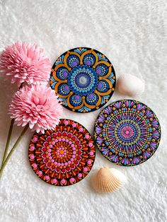 three coasters with designs on them next to a pink flower and seashell in the foreground