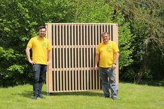 two men in yellow shirts standing next to a large wooden structure on the side of a field