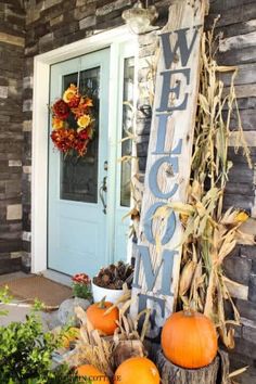 a welcome sign sitting in front of a door with pumpkins and corn stalks around it