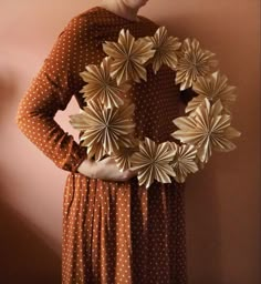 a woman standing next to a wall holding a paper wreath