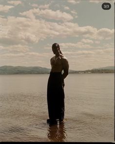 a woman is standing in the water with her hands on her head and looking off into the distance