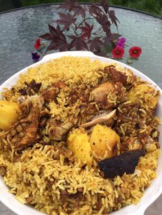 a white bowl filled with rice and meat on top of a table next to flowers