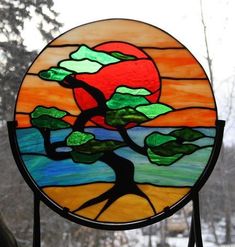 a stained glass window with a tree and sunset in the background, on a stand