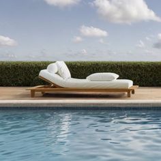 an empty chaise lounge next to a swimming pool in the day with blue sky and clouds