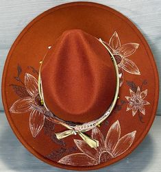 Burnt orange brown fedora with burned and hand painted flowers. Rustic Brown Felt Hat For Kentucky Derby, Brown Felt Hat For Kentucky Derby And Western Events, Handmade Brown Fedora For Fall, Brown Felt Hat For Western-themed Events And Kentucky Derby, Artisan Brown Hat Bands For Kentucky Derby, Custom Brown Felt Hat For Kentucky Derby, Brown Hand Painted Short Brim Hat, Artisan Brown Hat For Western-themed Events, Handmade Brown Felt Hat For Western-themed Events