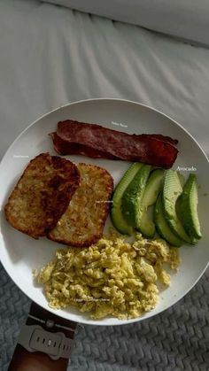 a person holding a plate with eggs, bacon and avocado slices on it