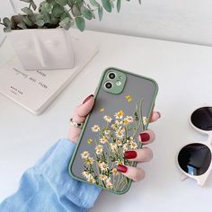 a woman holding up her phone case with daisies on it