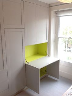 a white desk sitting in the corner of a room next to a window and cupboards