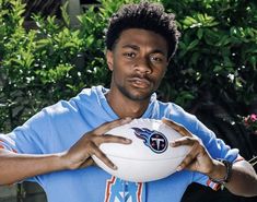 a young man holding a white football in his right hand and looking at the camera