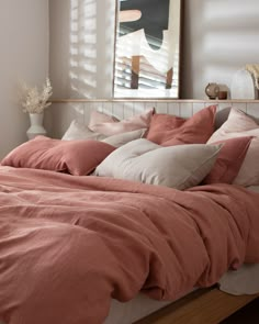 the bed is made with peach colored linens and pillows, along with a painting on the wall