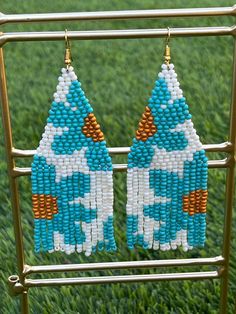 two blue and white beaded earrings hanging from a metal rack on grass covered ground