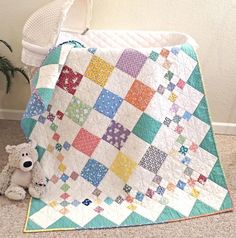 a teddy bear sitting next to a quilt on the floor