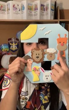 a woman holding up a cut out of a house with animals and bears on it