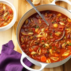 two bowls of soup are sitting on a wooden table next to bread and purple napkins