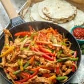 a skillet filled with chicken, peppers and tortilla bread on top of a table