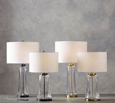 four clear glass table lamps with white linen shades on each lamp and one light in the middle