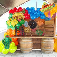 a table topped with lots of balloons and taco signs on top of wooden barrels