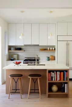 two stools sit in front of the kitchen island with bookshelves on it