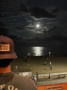 a man standing on top of a beach next to the ocean under a full moon