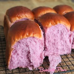 several pink buns sitting on top of a cooling rack next to each other, with one cut in half