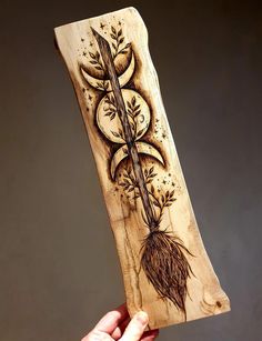 a hand holding a piece of wood with an image of a plant and moon on it