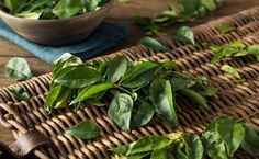 some green leaves sitting on top of a wicker table next to a bowl and spoon