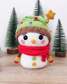 a crocheted snowman with a green hat and scarf on top of a wooden table