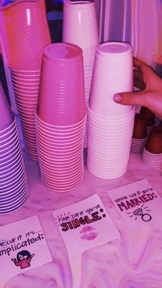 there are many pink and purple cups on the table with matching stickers around them