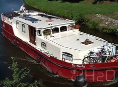 a red and white boat traveling down a river next to lush green grass covered banks