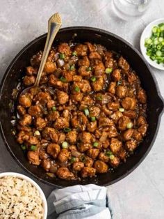 a skillet filled with meat and rice next to two bowls of sauce, chopsticks and green onions