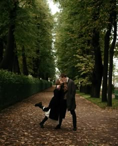 a man and woman kissing in the middle of a leaf covered path surrounded by trees