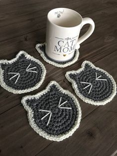 three crocheted coasters sitting on top of a wooden table next to a coffee cup