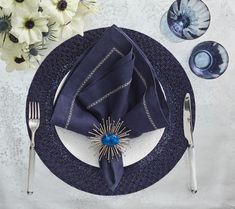 a place setting with blue napkins, silverware and flowers on the tablecloth