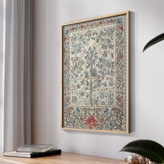 a framed tapestry hanging on the wall above a table with a book and potted plant