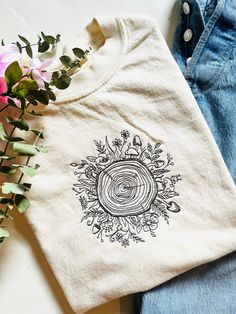 a white t - shirt with an image of a tree ring on it next to some flowers