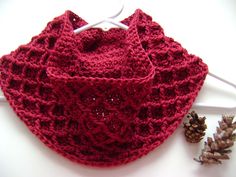 a red crocheted scarf sitting on top of a table next to pine cones