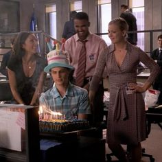 a group of people standing around a table with a birthday cake on top of it