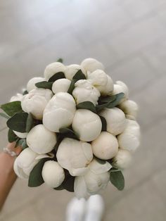 a bouquet of white flowers is held by someone's hand on a tile floor