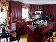 a kitchen with red cabinets and black counter tops is pictured in this image, there are four chairs around the island