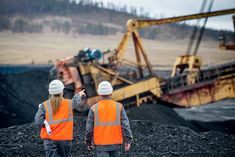 two construction workers in orange vests and hard hats looking at an excavator