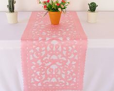 a pink table runner with flowers and cacti in pots on the top, along with two succulents