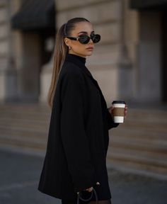 a woman in black is holding a coffee cup and looking off to the side with her hand on her hip