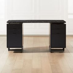 a black desk with two drawers on it in front of a white wall and hardwood floor