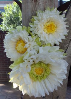 some white and yellow flowers are hanging from a wooden post in front of a brick wall