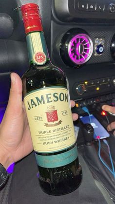 a person holding a bottle of wine in their hand next to a car steering wheel