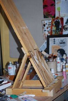 an easel sitting on top of a wooden table covered in paint and other art supplies