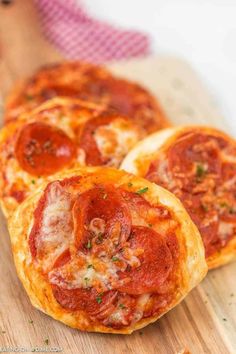 three pepperoni pizzas sitting on top of a wooden cutting board next to a slice of bread