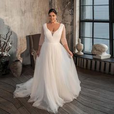 a woman in a white wedding dress standing on a wooden floor next to a window