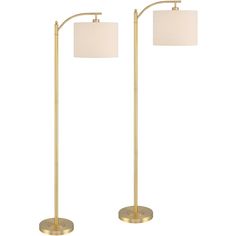 two gold floor lamps with white shades on them