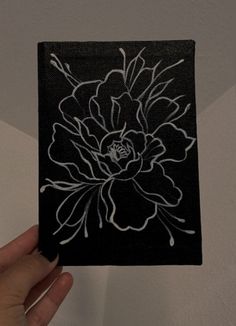 a hand holding up a black and white flower on a square piece of paper that has been drawn onto it